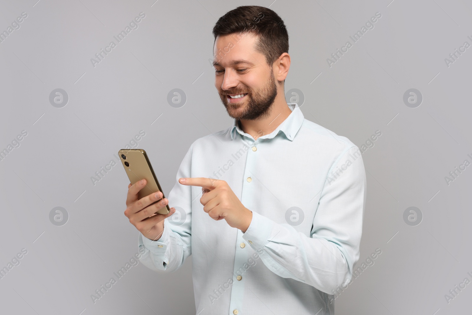 Photo of Happy man sending message via smartphone on grey background