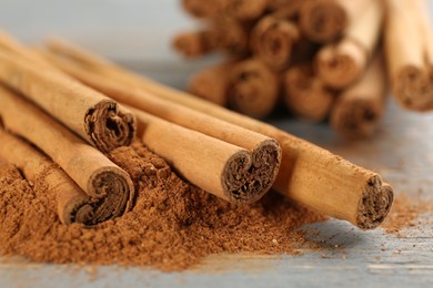 Photo of Aromatic cinnamon sticks and powder on grey wooden table, closeup