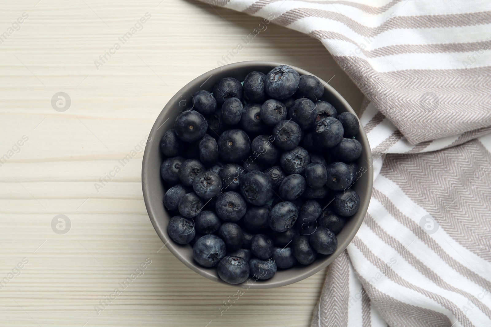 Photo of Ceramic bowl with blueberries and napkin on white wooden table, flat lay. Cooking utensil