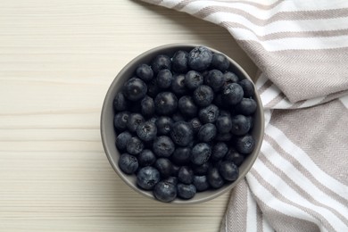 Ceramic bowl with blueberries and napkin on white wooden table, flat lay. Cooking utensil