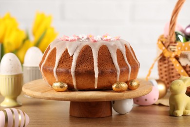 Delicious Easter cake decorated with sprinkles near eggs and rabbit figure on wooden table, closeup