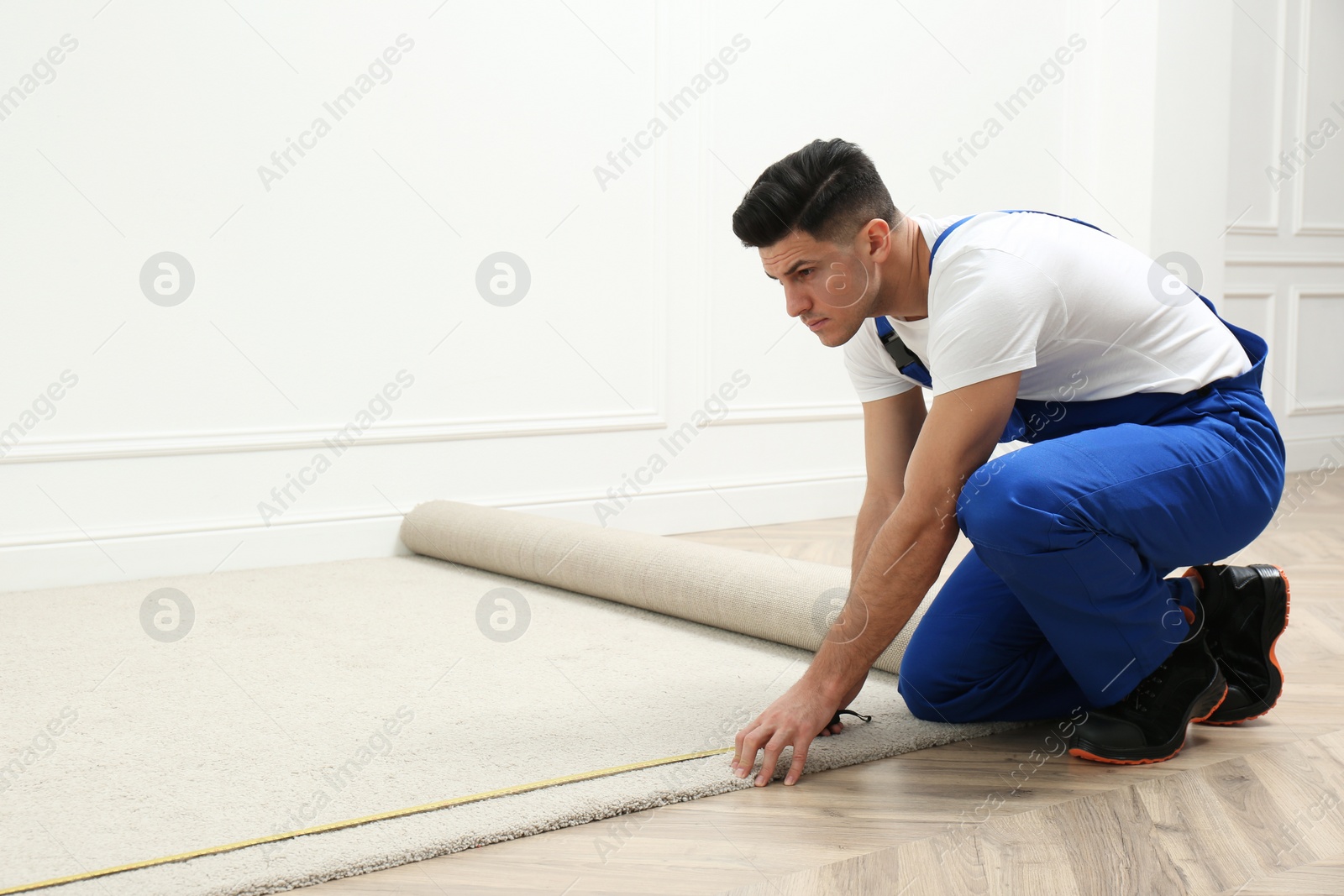 Photo of Worker with measuring tape installing new carpet indoors