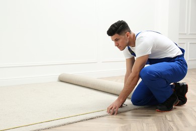 Photo of Worker with measuring tape installing new carpet indoors