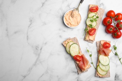 Photo of Tasty crispbreads with prosciutto, cream cheese and vegetables on white marble table, flat lay. Space for text