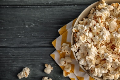 Photo of Bowl of tasty popcorn on wooden table, top view