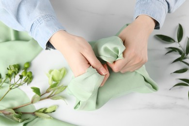 Photo of Furoshiki technique. Woman wrapping gift in green fabric at white table, top view