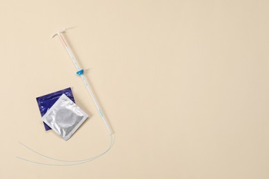 Contraception choice. Condoms and intrauterine device on beige background, flat lay. Space for text