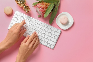 Photo of Woman using computer keyboard on table decorated with tropical flower, top view. Creative design ideas