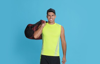 Handsome man with sports bag on light blue background