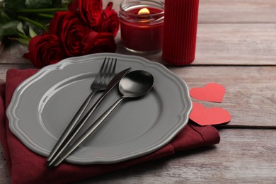 Photo of Romantic place setting with red roses, candle and decorative hearts on wooden table. St. Valentine's day dinner