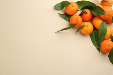 Photo of Fresh ripe tangerines with green leaves on beige background, flat lay. Space for text