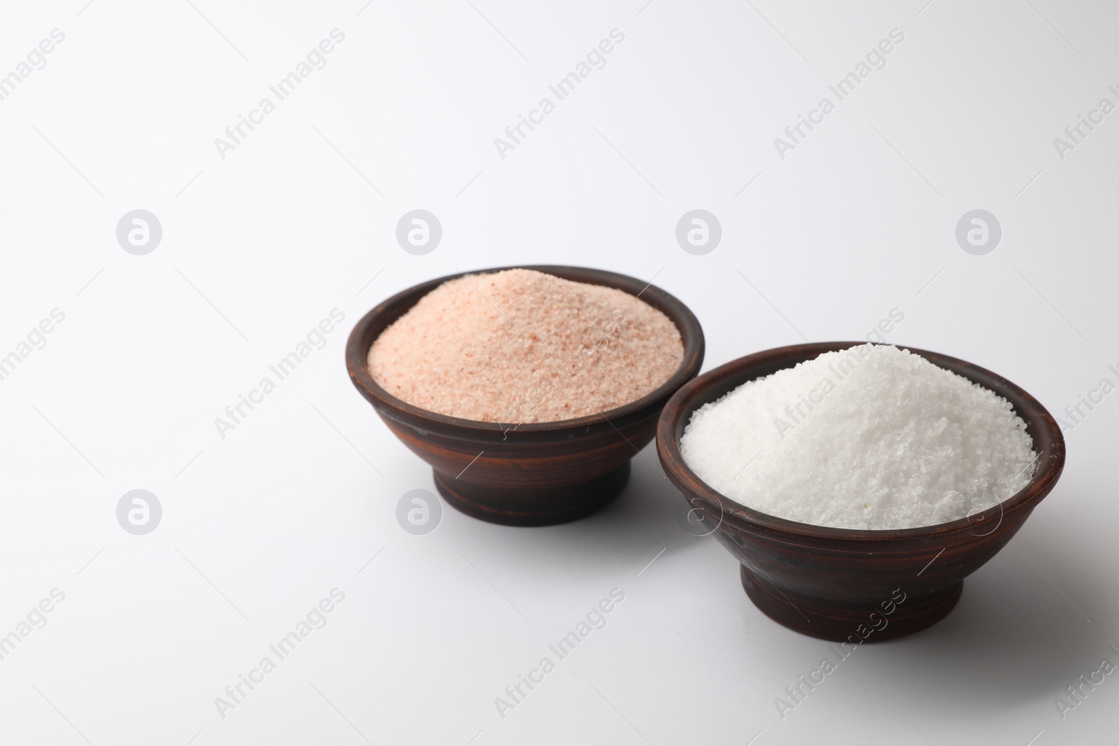 Photo of Different types of natural salt in bowls on white background, space for text