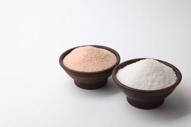 Photo of Different types of natural salt in bowls on white background, space for text