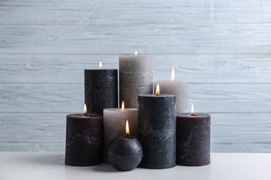 Set of burning candles on table against light wooden background