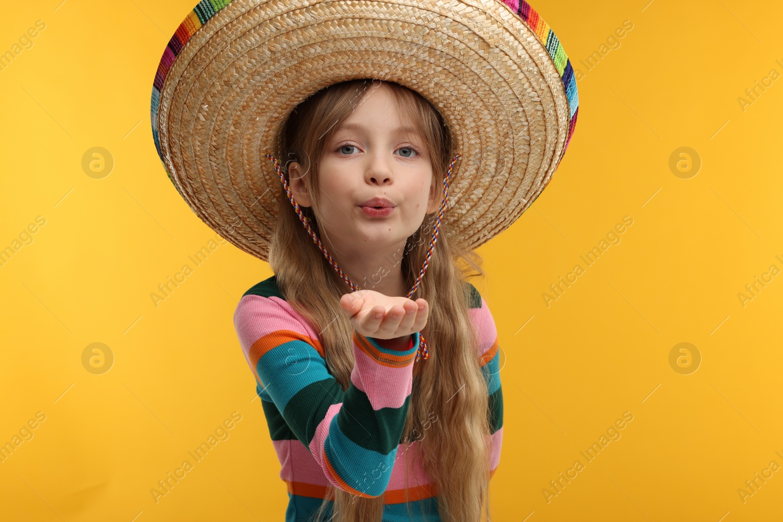 Photo of Cute girl in Mexican sombrero hat blowing kiss on orange background