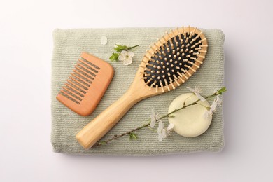Photo of Wooden hairbrush, solid shampoo, comb, towel and branch with flowers on white background, top view
