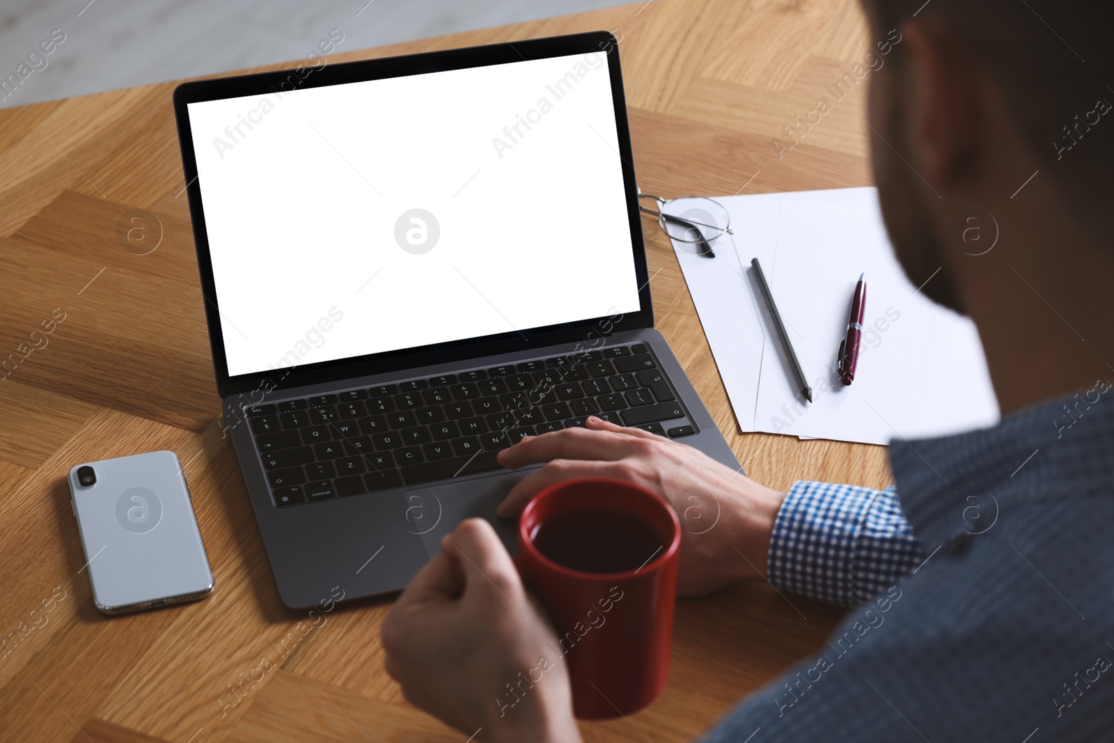 Photo of Man with cup of drink working on laptop at wooden desk, closeup