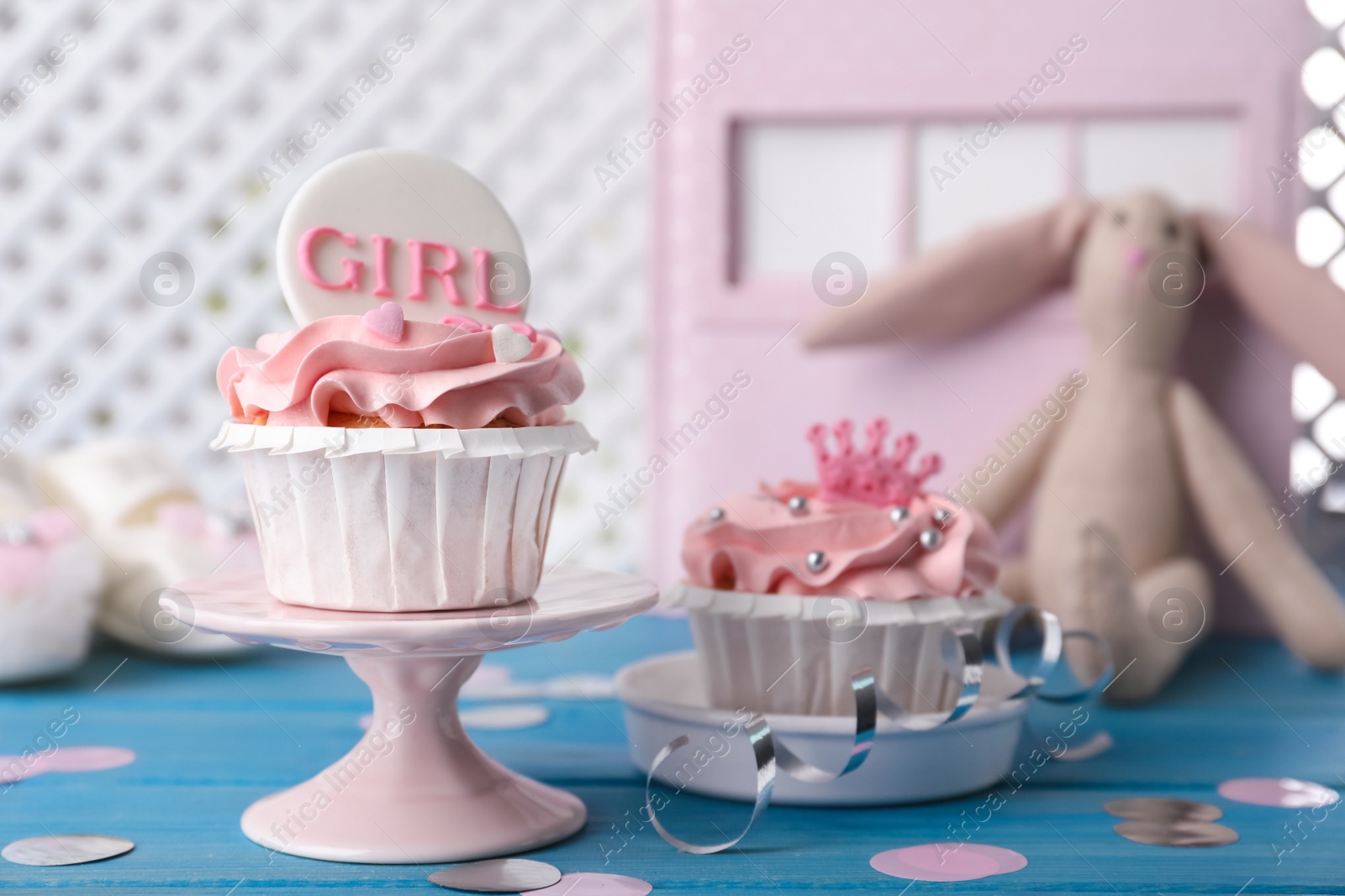 Photo of Delicious cupcakes with pink cream and toppers for baby shower on light blue wooden table