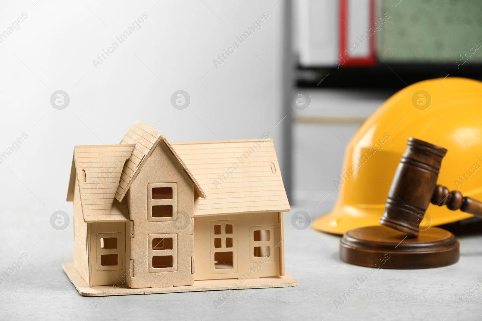 Photo of Construction and land law concepts. House model, gavel and hard hat on white table indoors