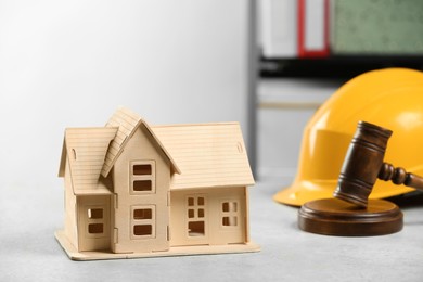 Construction and land law concepts. House model, gavel and hard hat on white table indoors