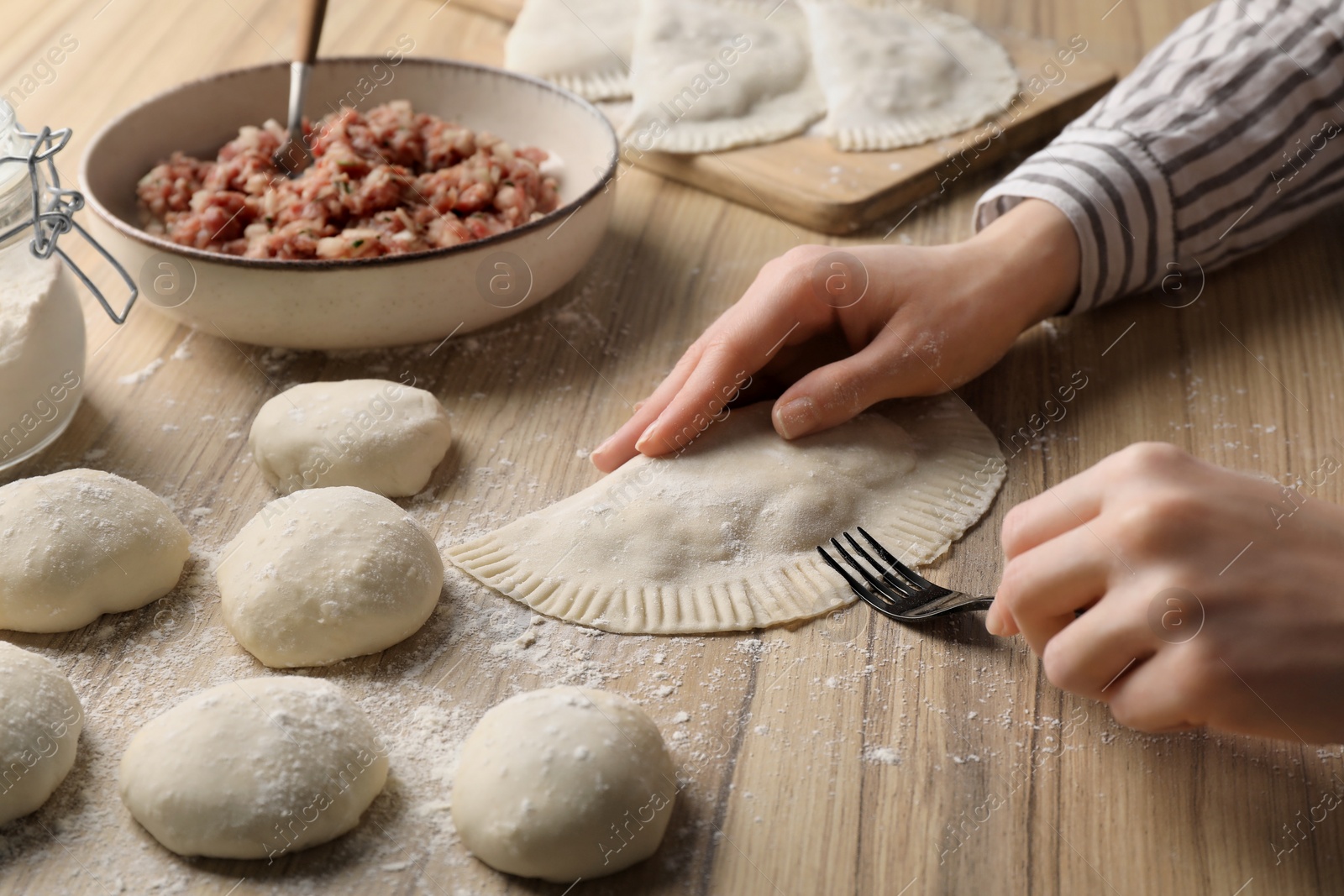 Photo of Woman making chebureki with tasty filling at wooden table, closeup