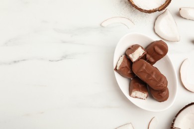 Photo of Delicious milk chocolate candy bars with coconut filling on white marble table, flat lay. Space for text