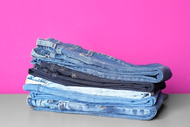 Stack of jeans on table against color background