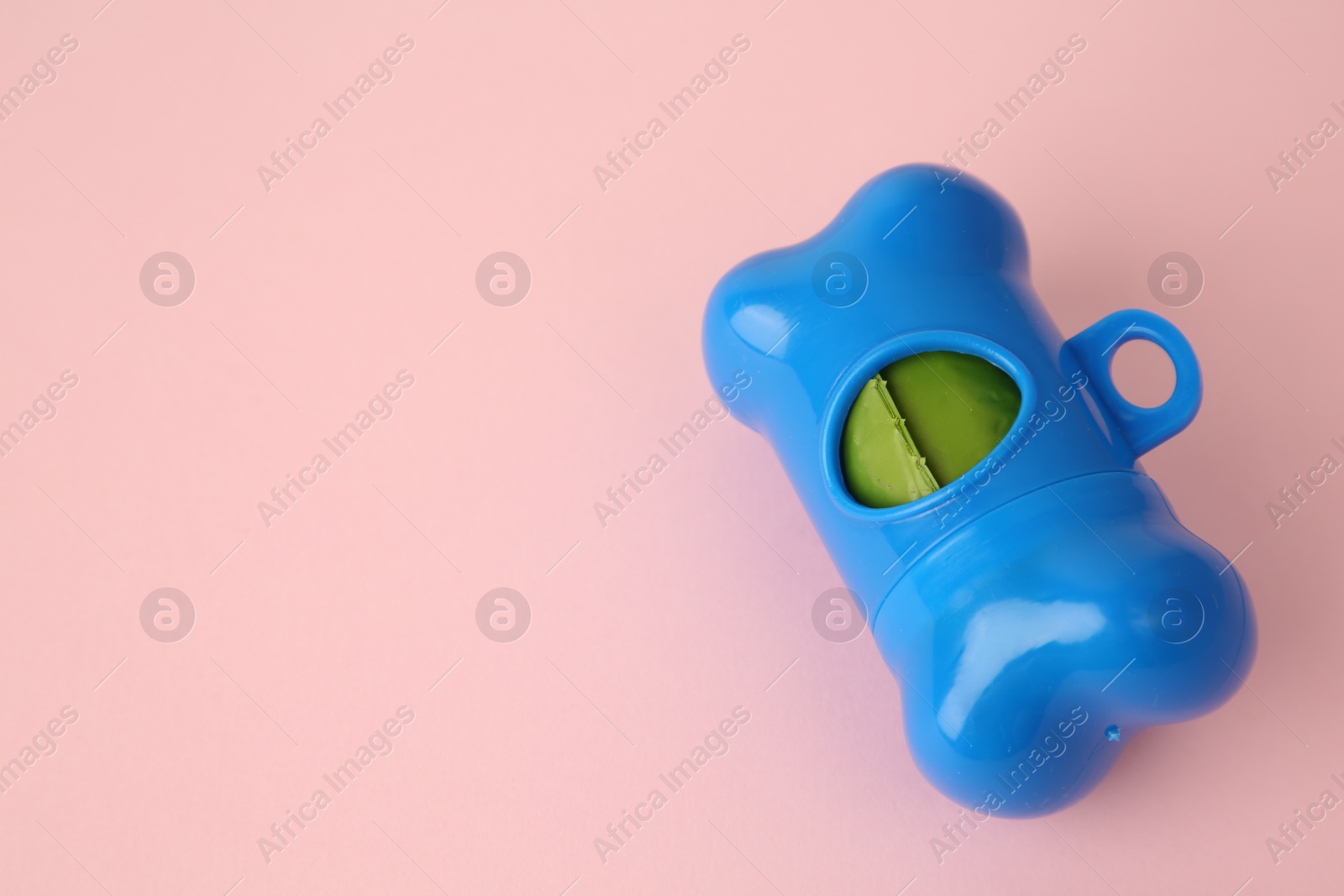 Photo of Dispenser with dog waste bags on pink background, closeup. Space for text