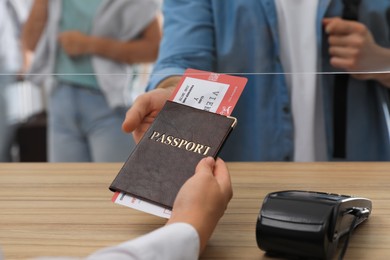Agent giving passport with ticket to client at check-in desk in airport, closeup