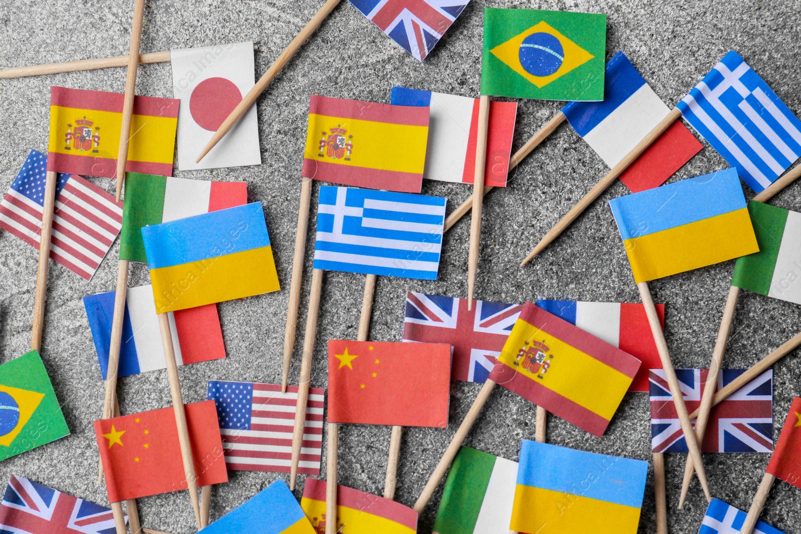 Photo of Many small paper flags of different countries on grey table, flat lay