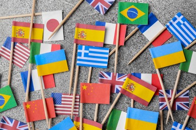 Photo of Many small paper flags of different countries on grey table, flat lay