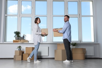 Photo of Happy couple with moving boxes near big window in new apartment