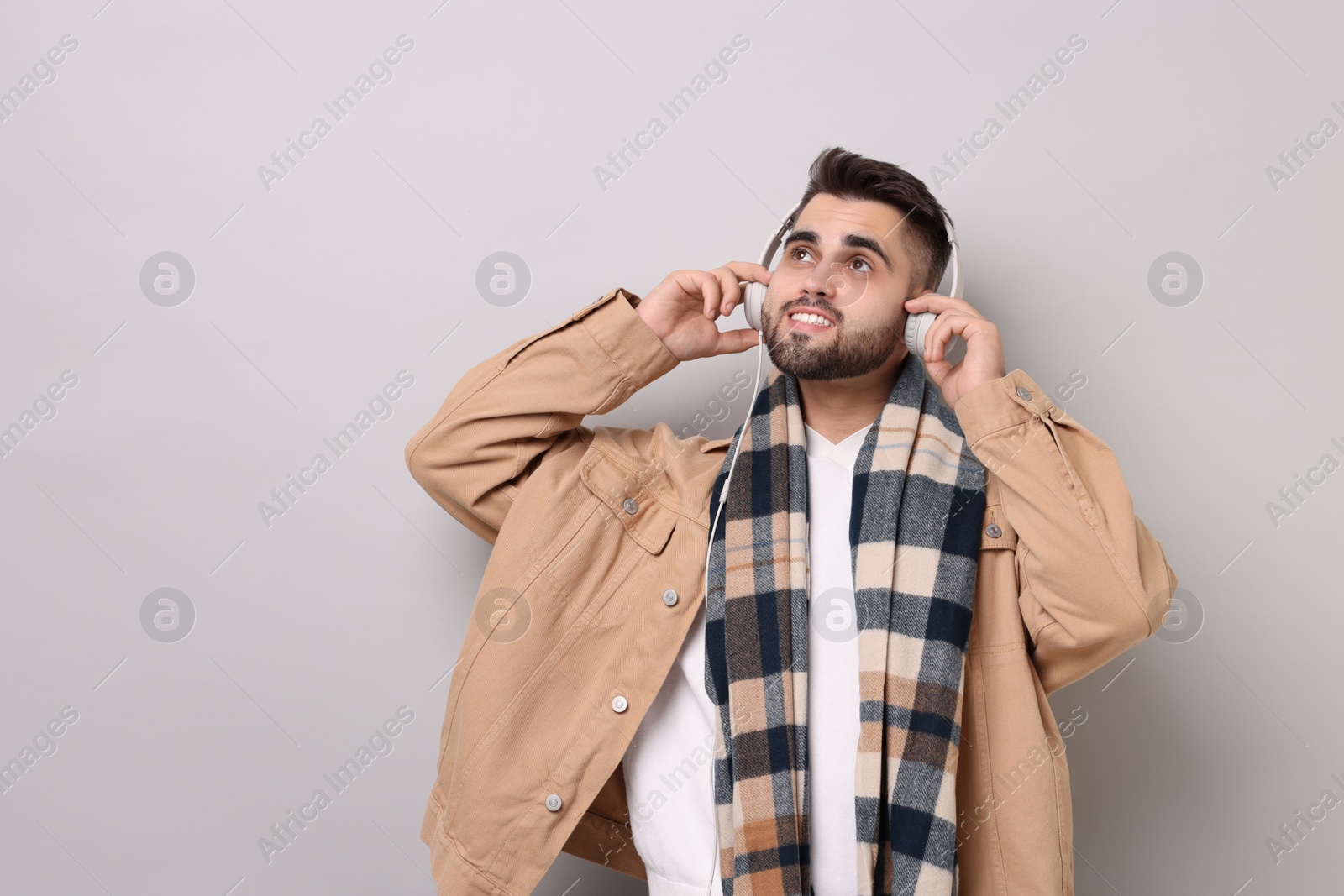 Photo of Smiling man in warm scarf listening to music on light grey background. Space for text