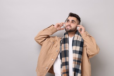 Smiling man in warm scarf listening to music on light grey background. Space for text