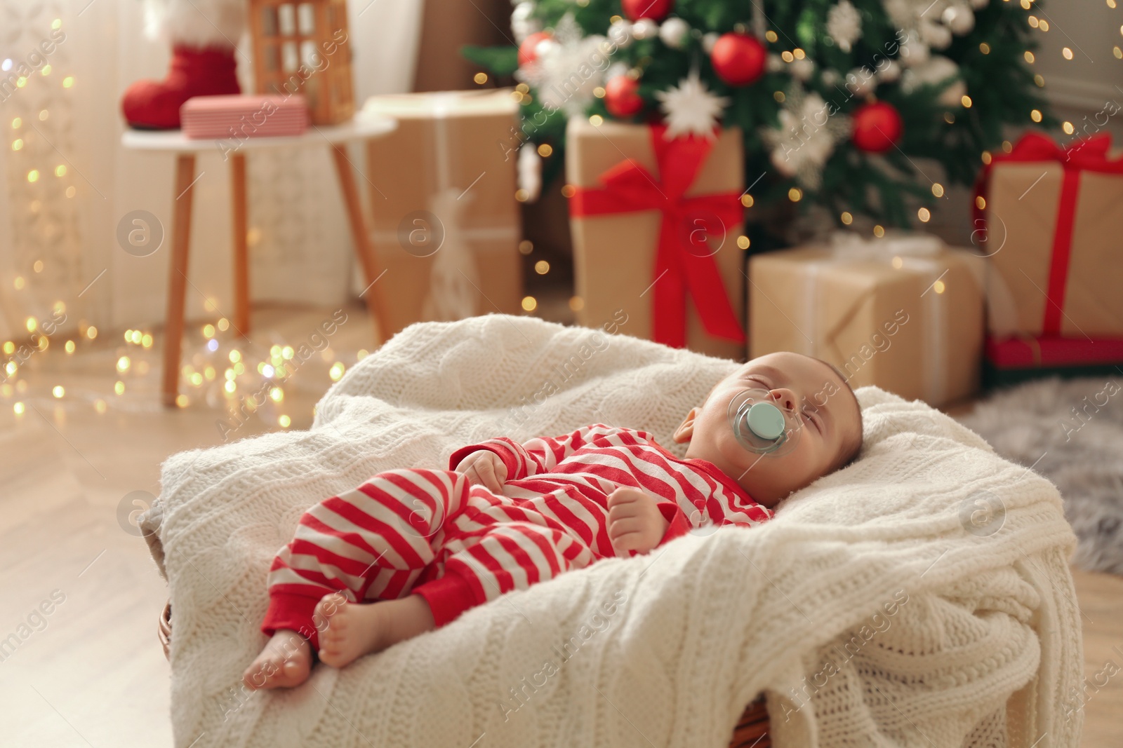 Photo of Cute little baby sleeping on knitted blanket in room decorated for Christmas