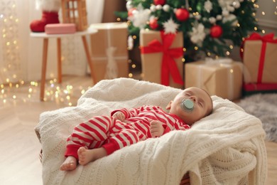 Cute little baby sleeping on knitted blanket in room decorated for Christmas
