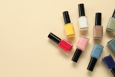 Colorful nail polishes in bottles on beige background, flat lay. Space for text