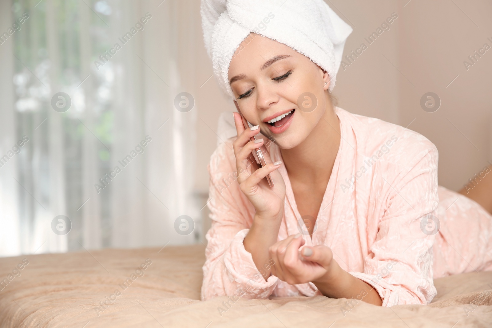 Photo of Beautiful woman with towel on head talking on phone in bedroom at home