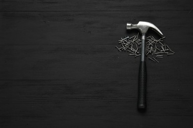 New hammer and metal nails on black wooden table, flat lay. Space for text