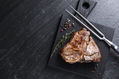 Photo of Delicious fried beef meat, thyme, peppercorns and fork on black table, top view. Space for text