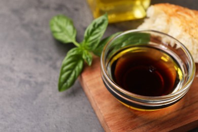 Photo of Bowl of organic balsamic vinegar with oil, basil and bread on grey table, closeup. Space for text