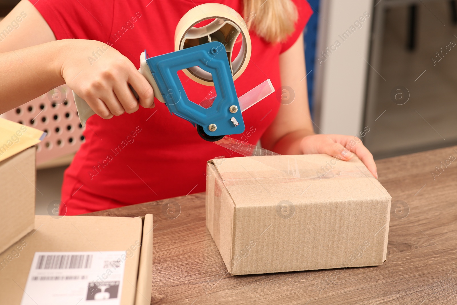 Photo of Post office worker packing parcel at counter indoors, closeup