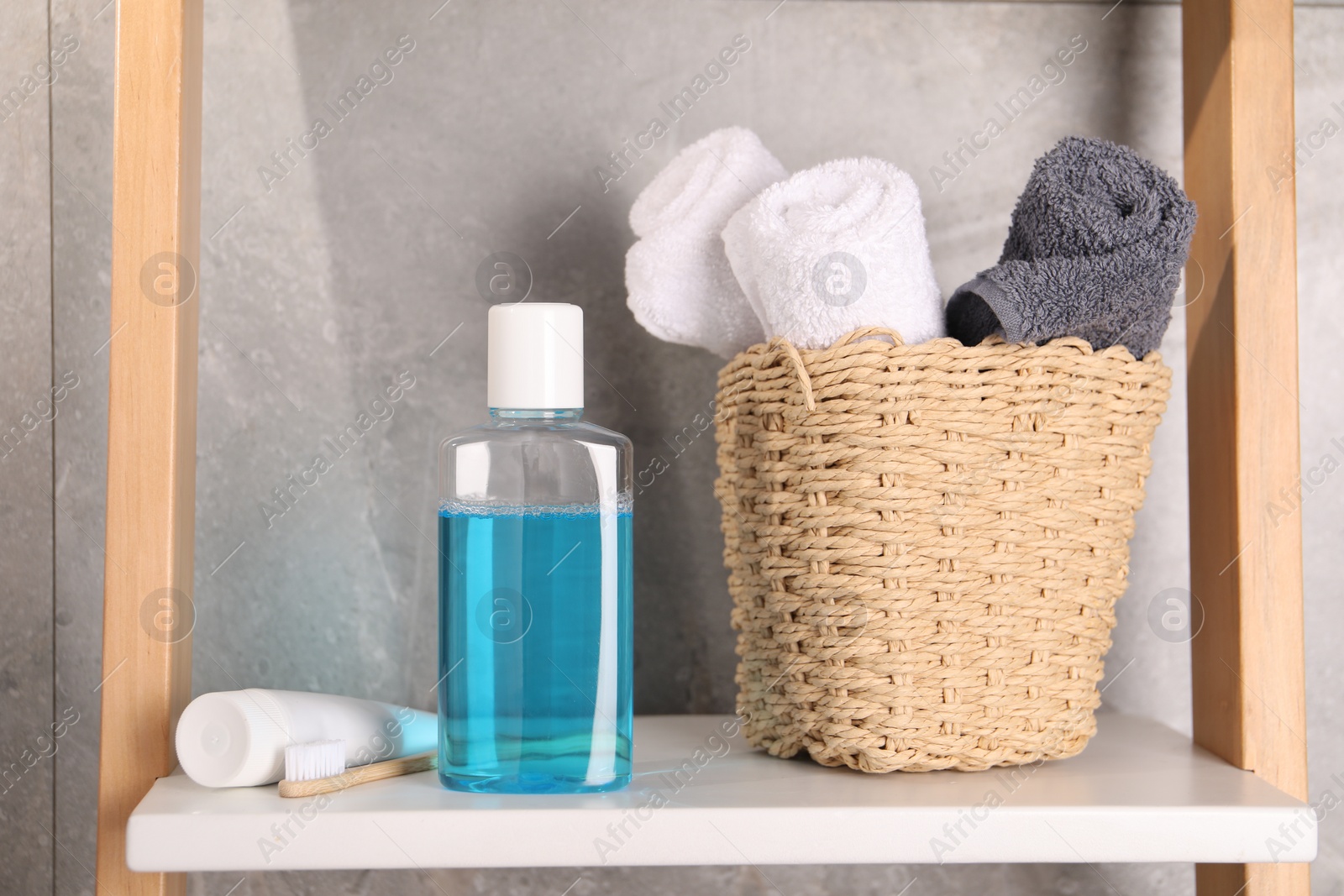 Photo of Bottle of mouthwash, toothpaste, toothbrush and towels on shelf in bathroom