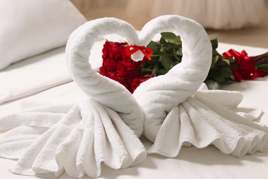 Honeymoon. Swans made of towels and beautiful red roses on bed in room