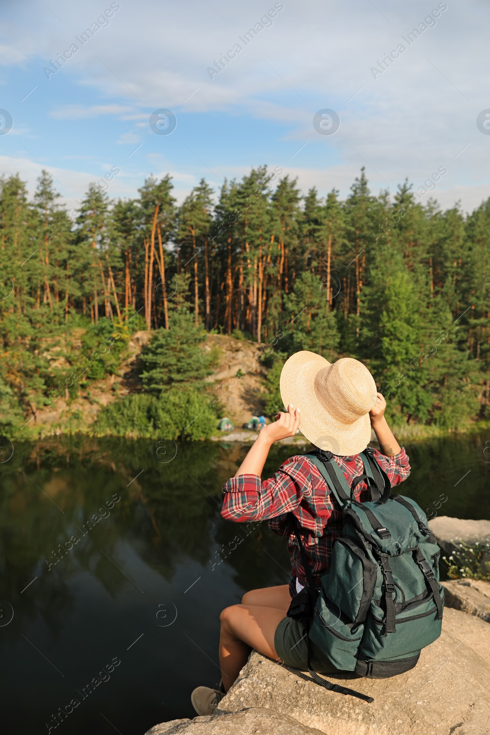 Photo of Young woman on rock near lake and forest. Camping season