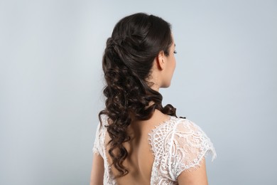 Young bride with beautiful wedding hairstyle on light grey background