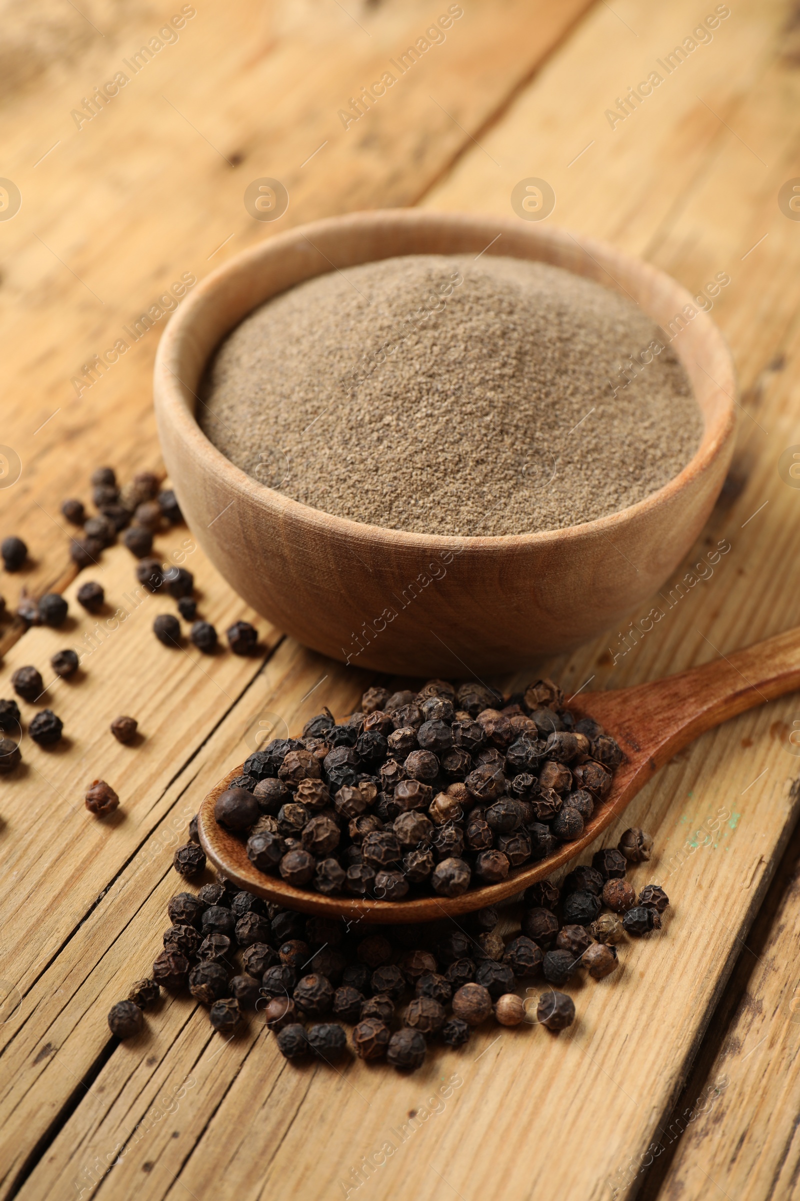 Photo of Aromatic spice. Ground and whole black pepper on wooden table, closeup