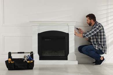 Photo of Man with screwdriver installing electric fireplace in room