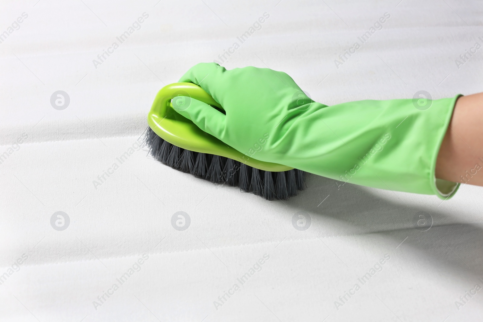 Photo of Woman in green gloves cleaning white mattress with brush, closeup