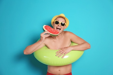 Shirtless man with inflatable ring eating watermelon on color background